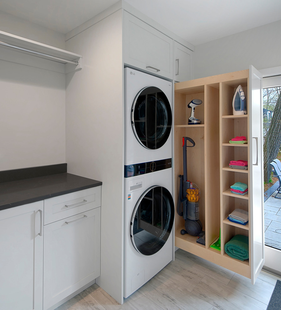 Inspiration for a small modern single-wall dedicated laundry room in Chicago with raised-panel cabinets, white cabinets, quartz benchtops, white walls, porcelain floors, a stacked washer and dryer, grey floor and grey benchtop.