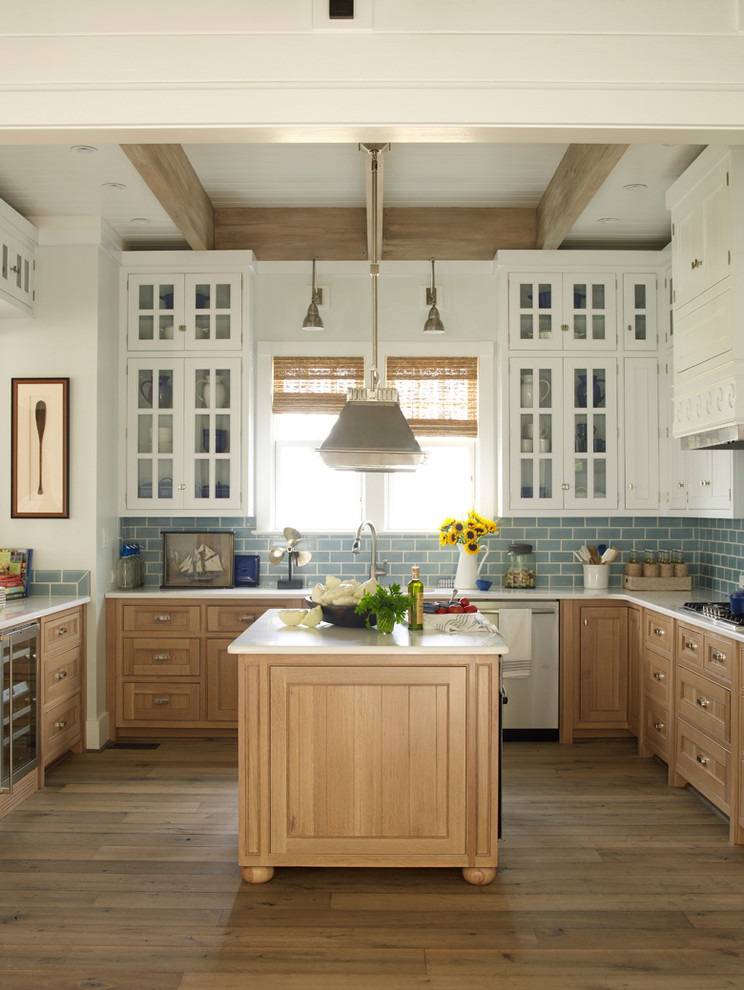 Inspiration for a beach style kitchen in Jacksonville with marble benchtops, blue splashback, subway tile splashback, stainless steel appliances, light hardwood floors, with island, glass-front cabinets and white cabinets.