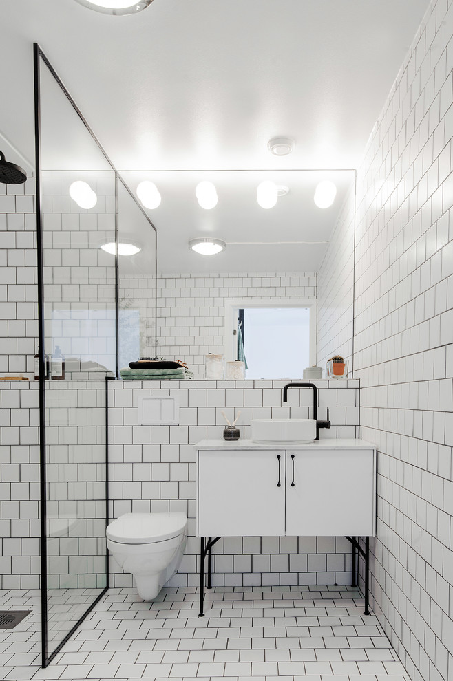 Photo of a mid-sized scandinavian bathroom in Stockholm with white cabinets, a wall-mount toilet, white tile, porcelain tile, white walls, porcelain floors, a vessel sink and marble benchtops.