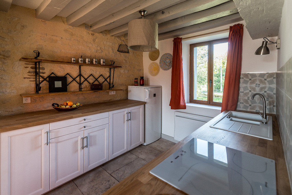 Mid-sized country galley open plan kitchen in Paris with an undermount sink, recessed-panel cabinets, light wood cabinets, wood benchtops, beige splashback, cement tile splashback, white appliances, no island and beige floor.