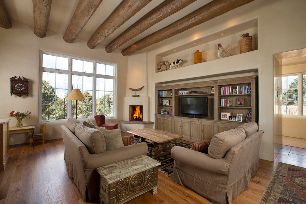 Mid-sized mediterranean open concept family room in Albuquerque with beige walls, medium hardwood floors, a corner fireplace, a freestanding tv, a library and a plaster fireplace surround.