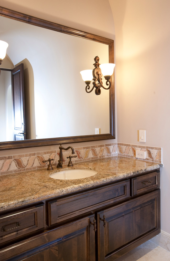 This is an example of an expansive mediterranean 3/4 bathroom in Houston with a drop-in sink, raised-panel cabinets, dark wood cabinets, marble benchtops, a two-piece toilet, beige tile, stone tile, beige walls, travertine floors and an alcove shower.