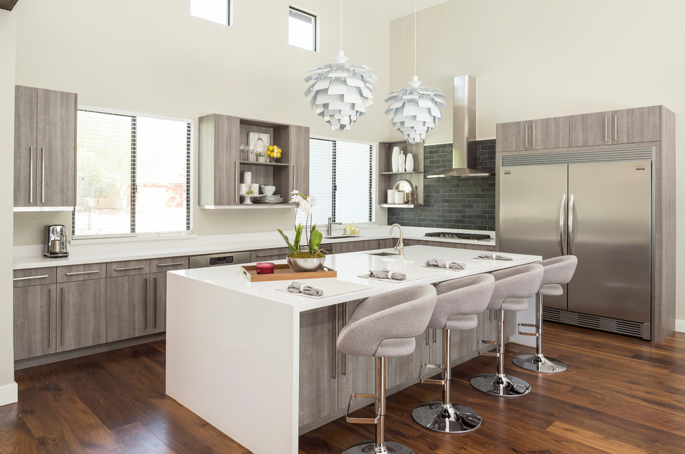 This is an example of a mid-sized contemporary galley open plan kitchen in Phoenix with an undermount sink, flat-panel cabinets, grey cabinets, quartzite benchtops, black splashback, slate splashback, stainless steel appliances, medium hardwood floors, with island and brown floor.