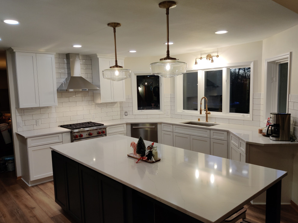 Example of a mid-sized minimalist u-shaped vinyl floor and brown floor eat-in kitchen design in Milwaukee with an undermount sink, shaker cabinets, white cabinets, quartz countertops, white backsplash, porcelain backsplash, stainless steel appliances, an island and white countertops