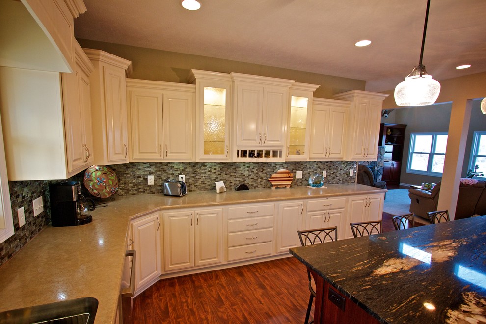 Example of a large u-shaped medium tone wood floor open concept kitchen design with a drop-in sink, raised-panel cabinets, white cabinets, multicolored backsplash, glass tile backsplash, stainless steel appliances and an island