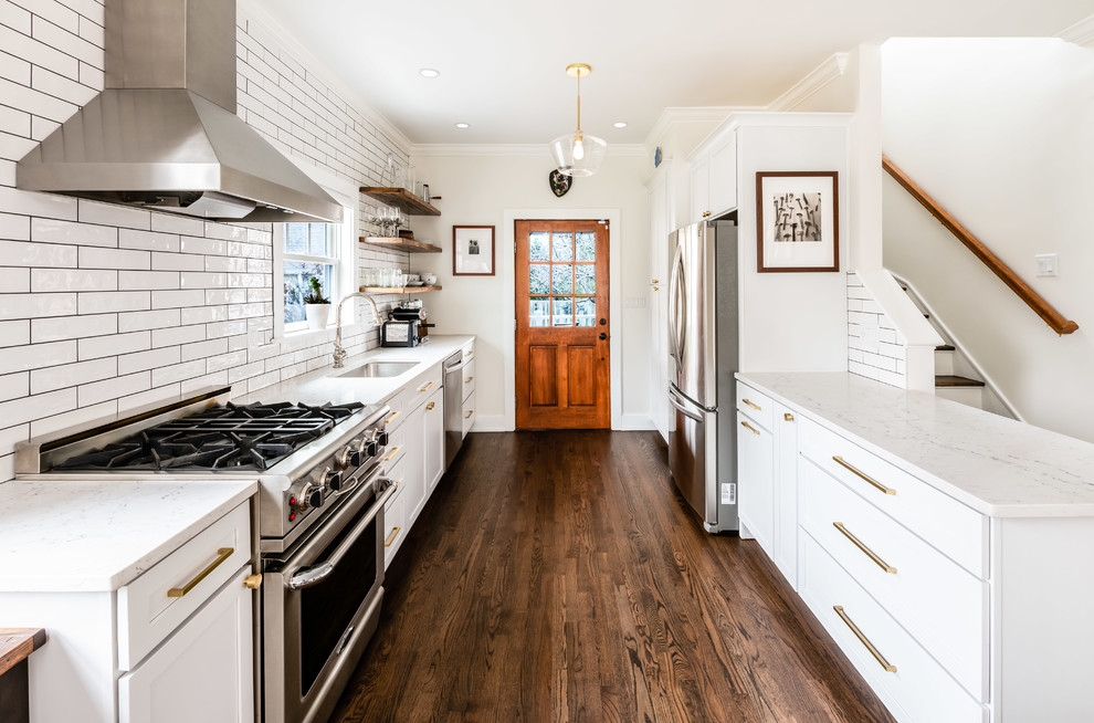 Transitional galley kitchen in DC Metro with an undermount sink, shaker cabinets, white cabinets, white splashback, subway tile splashback, stainless steel appliances, dark hardwood floors, a peninsula, brown floor and white benchtop.