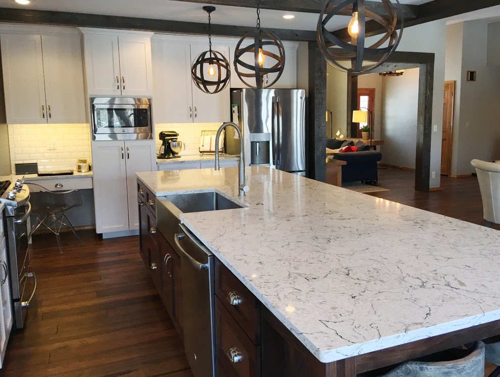 Inspiration for a large country l-shaped eat-in kitchen in Other with a farmhouse sink, shaker cabinets, white cabinets, quartz benchtops, white splashback, subway tile splashback, stainless steel appliances, dark hardwood floors and with island.