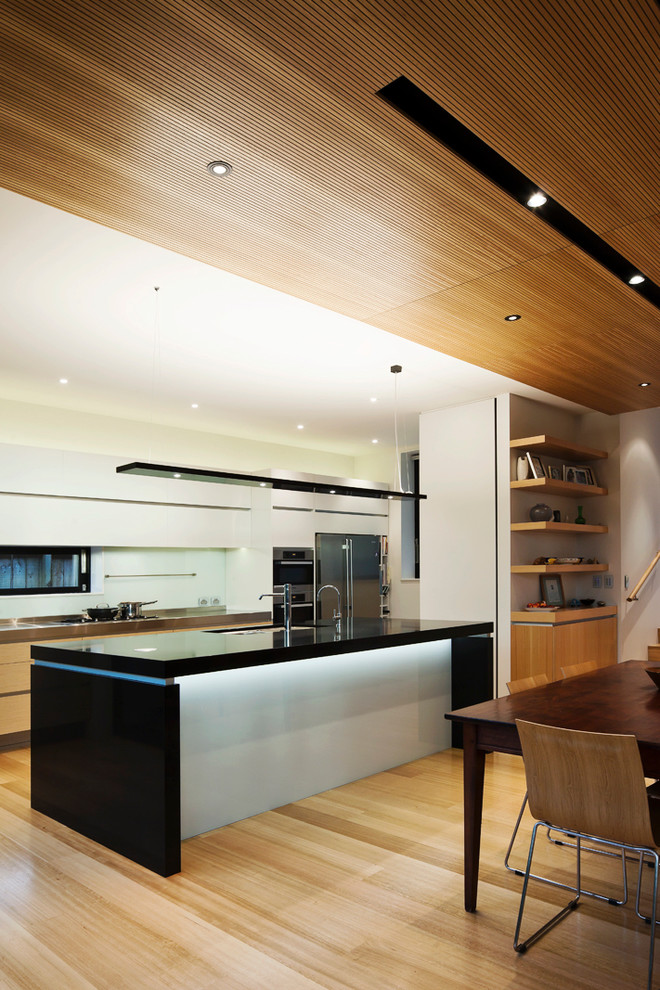 Photo of a mid-sized contemporary single-wall eat-in kitchen in Auckland with an undermount sink, recessed-panel cabinets, white cabinets, granite benchtops, blue splashback, glass sheet splashback, stainless steel appliances, medium hardwood floors and with island.