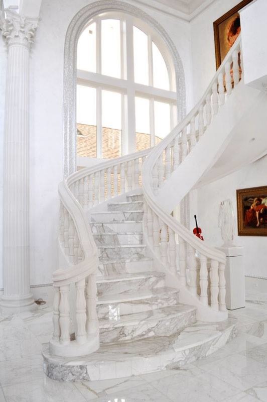 This is an example of a large mediterranean marble curved staircase in Kansas City with marble risers and wood railing.
