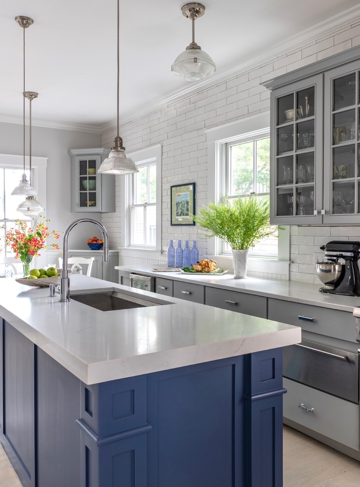 Inspiration for a large beach style eat-in kitchen in Boston with an undermount sink, grey cabinets, quartz benchtops, white splashback, stainless steel appliances, with island, white benchtop, glass-front cabinets, subway tile splashback and light hardwood floors.
