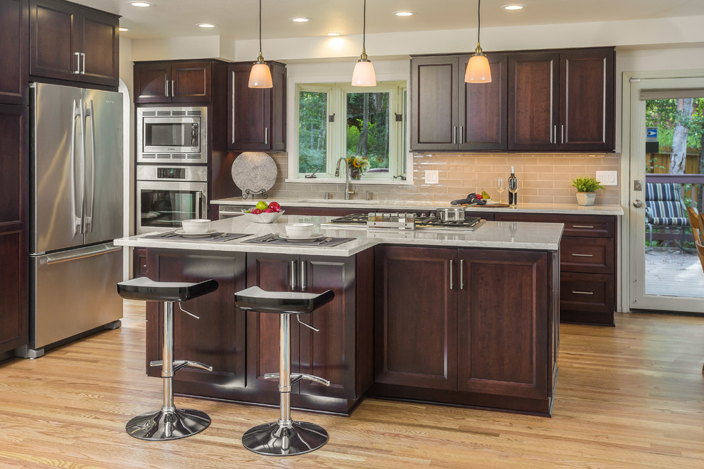 Mid-sized transitional l-shaped light wood floor open concept kitchen photo with an undermount sink, recessed-panel cabinets, dark wood cabinets, quartz countertops, gray backsplash, subway tile backsplash, stainless steel appliances and an island
