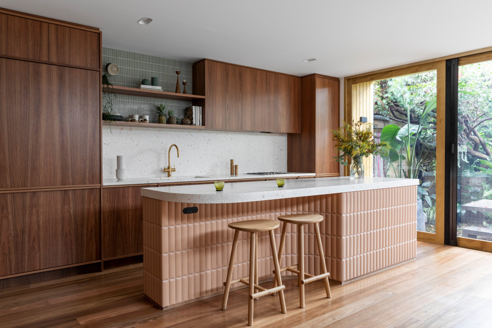 Inspiration for a small contemporary open plan kitchen in Sydney with an undermount sink, medium wood cabinets, terrazzo benchtops, pink splashback, stone slab splashback, black appliances, medium hardwood floors, with island, brown floor and pink benchtop.