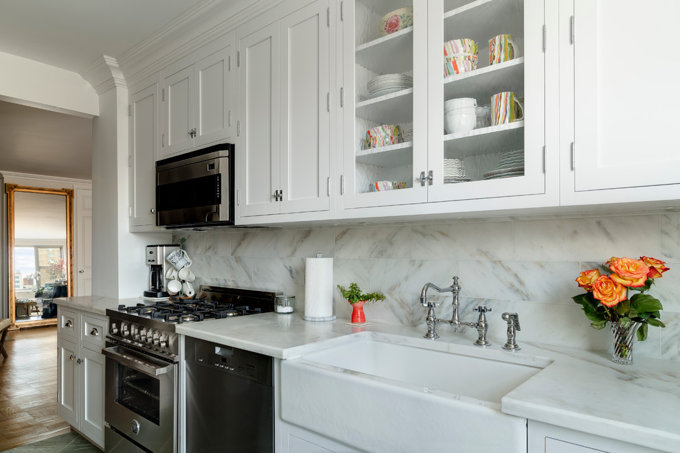 Photo of a small transitional galley separate kitchen in New York with a farmhouse sink, recessed-panel cabinets, white cabinets, marble benchtops, white splashback, stone tile splashback, stainless steel appliances, slate floors and no island.