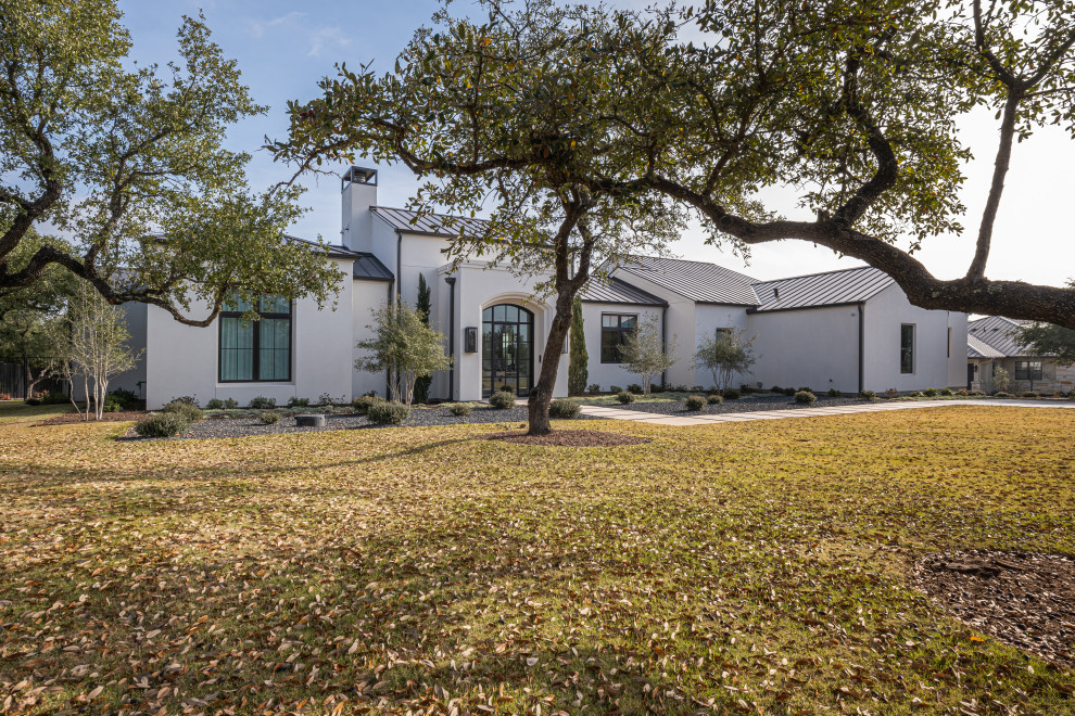 Photo of a large contemporary one-storey white house exterior in Austin with a gable roof and a metal roof.