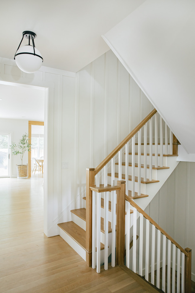 Diseño de escalera en L costera grande con escalones de madera, contrahuellas de madera pintada, barandilla de madera y panelado