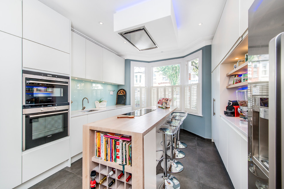 Photo of a mid-sized contemporary galley separate kitchen in London with an undermount sink, flat-panel cabinets, white cabinets, blue splashback, glass sheet splashback, stainless steel appliances and with island.