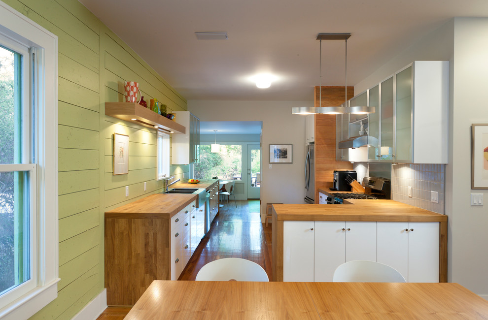 Contemporary u-shaped eat-in kitchen in Austin with a farmhouse sink, flat-panel cabinets, white cabinets, wood benchtops, white splashback and stainless steel appliances.