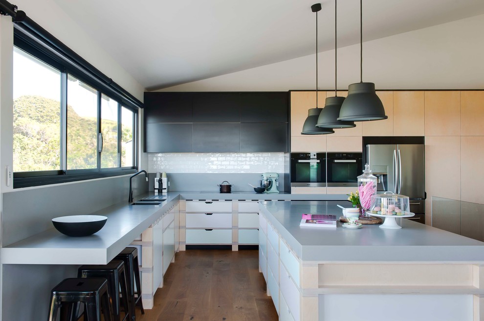 This is an example of a large contemporary l-shaped kitchen in Sydney with an undermount sink, flat-panel cabinets, light wood cabinets, solid surface benchtops, grey splashback, porcelain splashback, with island, stainless steel appliances and dark hardwood floors.