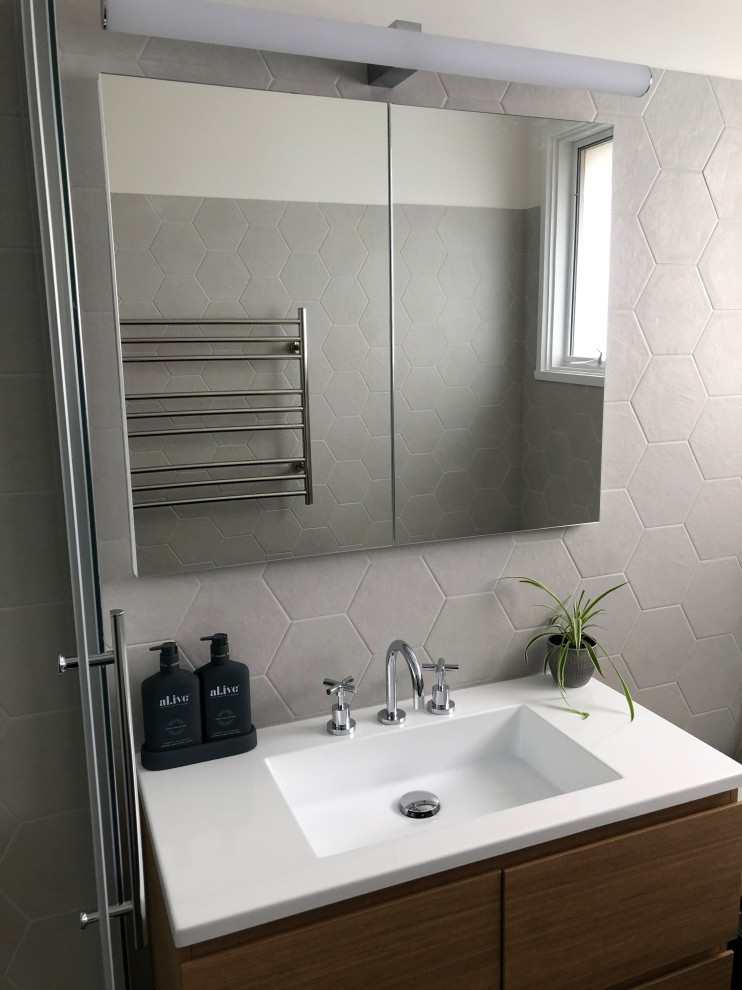 Photo of a small contemporary master bathroom in Other with flat-panel cabinets, light wood cabinets, a drop-in tub, a corner shower, gray tile, ceramic tile, grey walls, ceramic floors, an integrated sink, solid surface benchtops, black floor, a sliding shower screen, white benchtops, a single vanity and a floating vanity.
