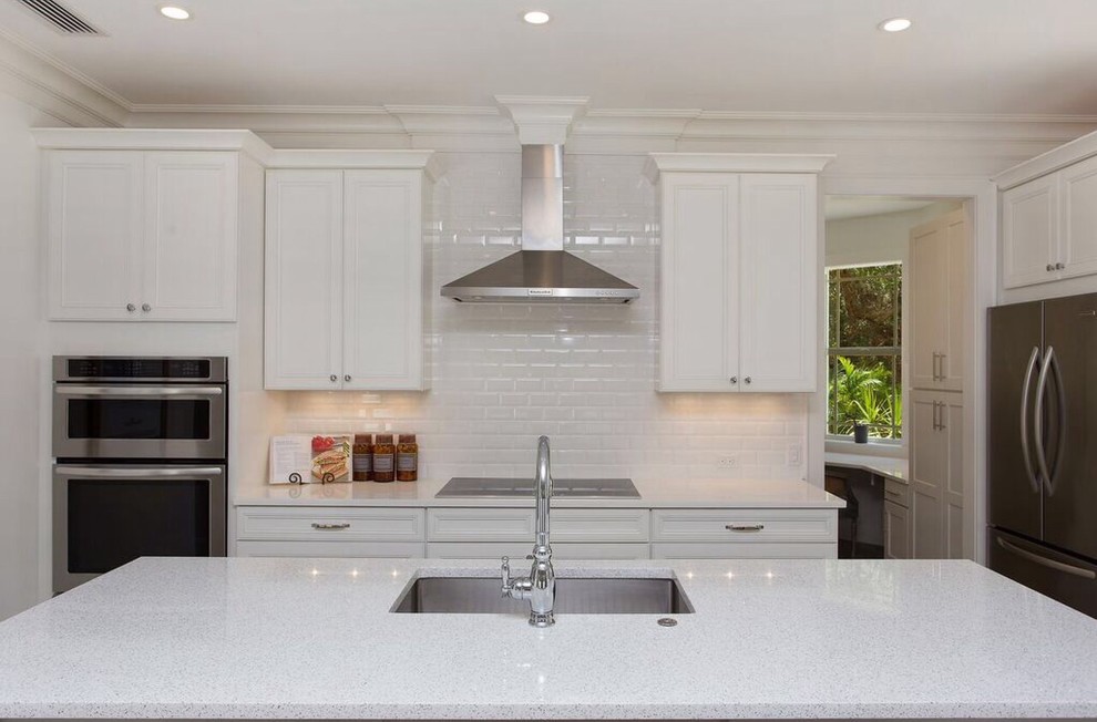 Inspiration for a large beach style eat-in kitchen in Tampa with light hardwood floors, an undermount sink, recessed-panel cabinets, white cabinets, white splashback, subway tile splashback, stainless steel appliances and with island.