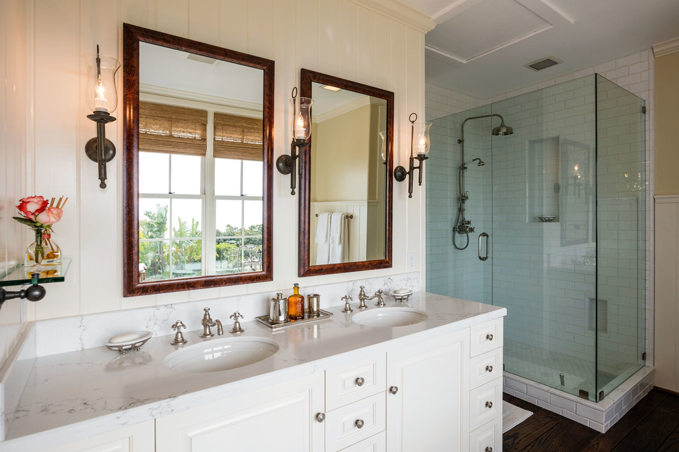 Photo of a traditional bathroom in Los Angeles with raised-panel cabinets, white cabinets, a corner shower, white tile, subway tile, dark hardwood floors and an undermount sink.