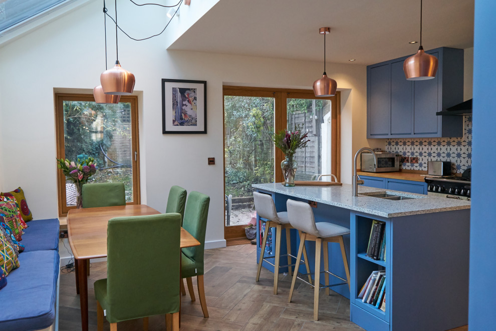 Inspiration for a large contemporary galley open plan kitchen in London with an integrated sink, flat-panel cabinets, blue cabinets, recycled glass benchtops, blue splashback, porcelain splashback, white appliances, light hardwood floors, with island, blue benchtop and vaulted.