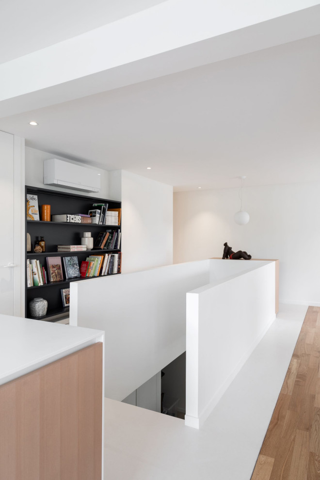 Esempio di un soggiorno minimal di medie dimensioni e aperto con libreria, pareti bianche, parquet chiaro e TV a parete
