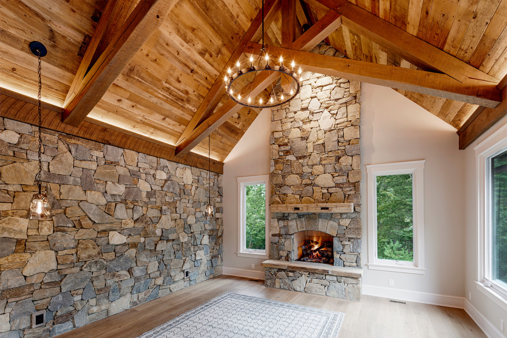 This is an example of a large rustic master bedroom in Other with grey walls, medium hardwood flooring, a standard fireplace, a stone fireplace surround, grey floors and exposed beams.