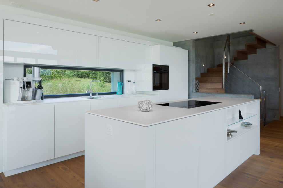 Inspiration for a contemporary kitchen in San Francisco with an undermount sink, flat-panel cabinets, white cabinets, window splashback, black appliances, medium hardwood floors and with island.