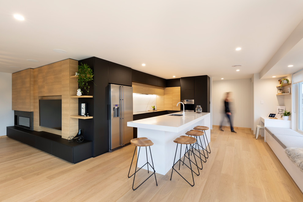 Photo of a large modern l-shaped eat-in kitchen in Other with an undermount sink, flat-panel cabinets, black cabinets, solid surface benchtops, white splashback, ceramic splashback, stainless steel appliances, light hardwood floors, with island and white benchtop.