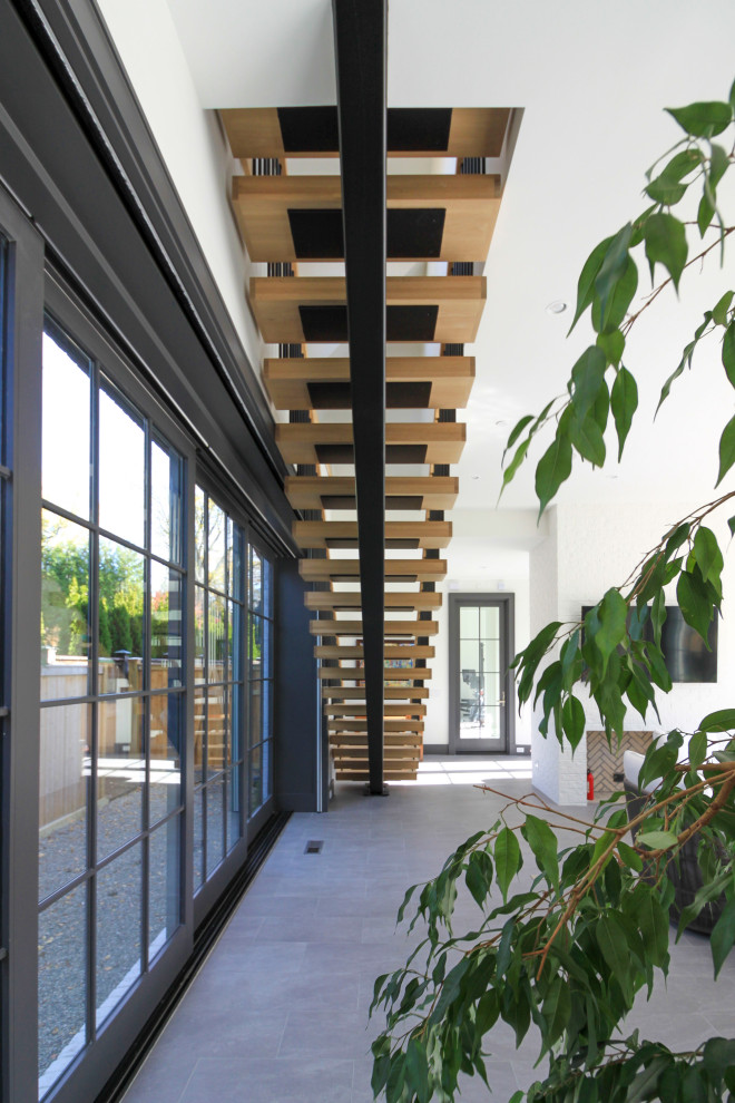 Foto di un'ampia scala sospesa minimalista con pedata in legno, parapetto in materiali misti e pareti in perlinato