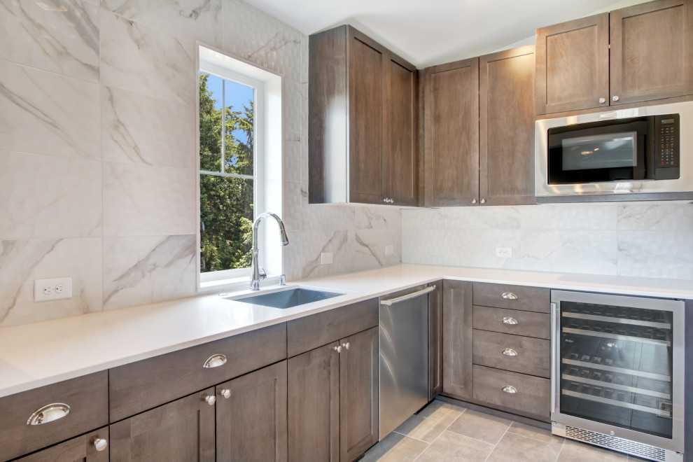 This is an example of a large contemporary l-shaped wet bar in Seattle with a drop-in sink, recessed-panel cabinets, dark wood cabinets, quartz benchtops, white splashback, porcelain splashback, ceramic floors, beige floor and white benchtop.