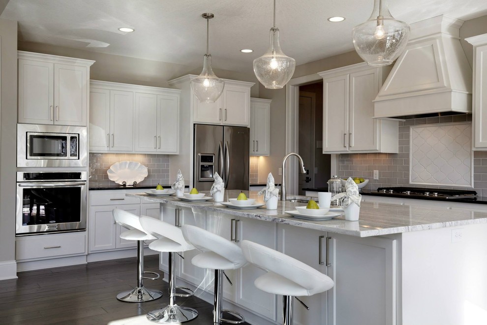 Example of a mid-sized transitional l-shaped dark wood floor open concept kitchen design in Minneapolis with a double-bowl sink, shaker cabinets, white cabinets, granite countertops, gray backsplash, subway tile backsplash, stainless steel appliances and an island