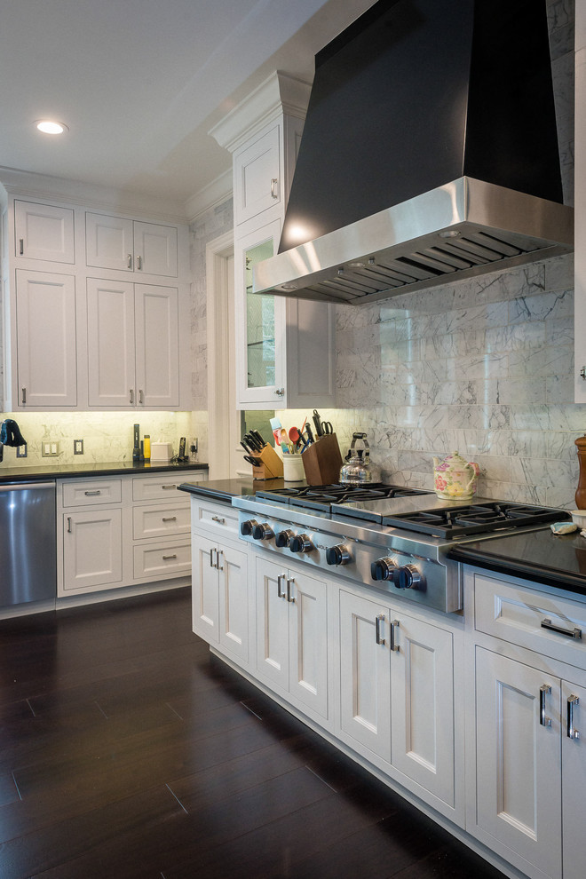 Mid-sized traditional u-shaped eat-in kitchen in Los Angeles with a farmhouse sink, raised-panel cabinets, white cabinets, soapstone benchtops, white splashback, marble splashback, stainless steel appliances, dark hardwood floors and with island.