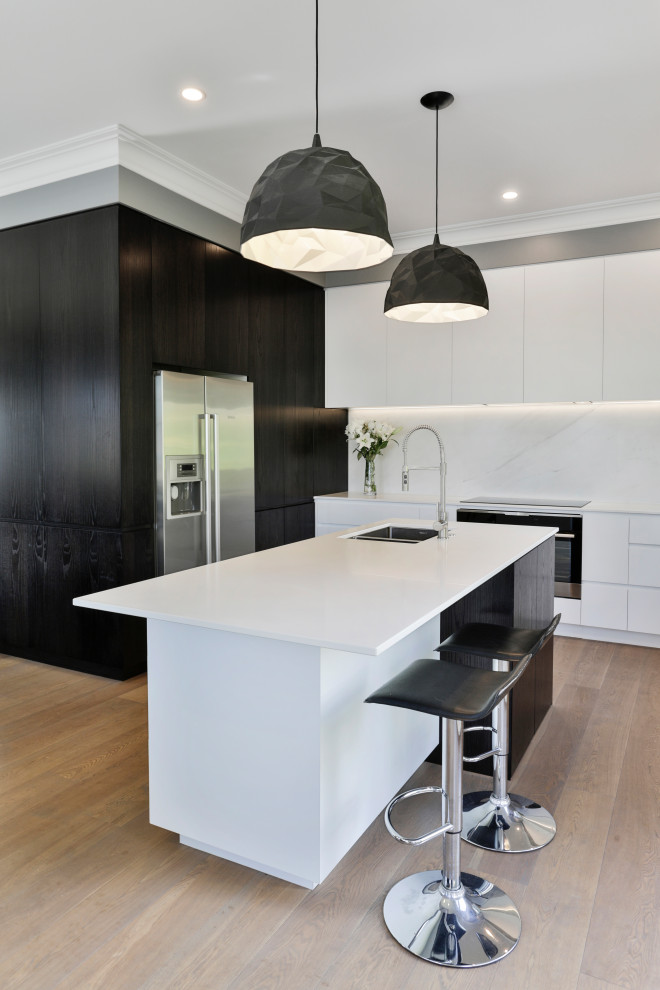 Photo of a mid-sized contemporary kitchen in Christchurch with an undermount sink, flat-panel cabinets, white cabinets, quartz benchtops, stainless steel appliances, with island, white benchtop, white splashback, stone slab splashback and light hardwood floors.