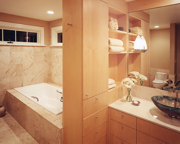 Photo of a mid-sized midcentury master bathroom in Seattle with a vessel sink, flat-panel cabinets, light wood cabinets, engineered quartz benchtops, a drop-in tub, an alcove shower, a one-piece toilet, beige tile, stone tile, brown walls and travertine floors.