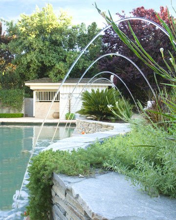 This is an example of a large country backyard rectangular lap pool in San Francisco with natural stone pavers and a water feature.