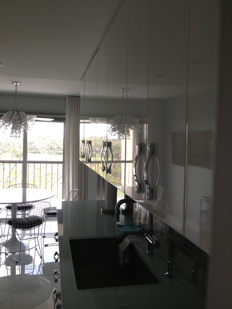 Photo of a mid-sized contemporary galley eat-in kitchen in Miami with an undermount sink, flat-panel cabinets, white cabinets, recycled glass benchtops, grey splashback, metal splashback, stainless steel appliances, ceramic floors, no island and white floor.