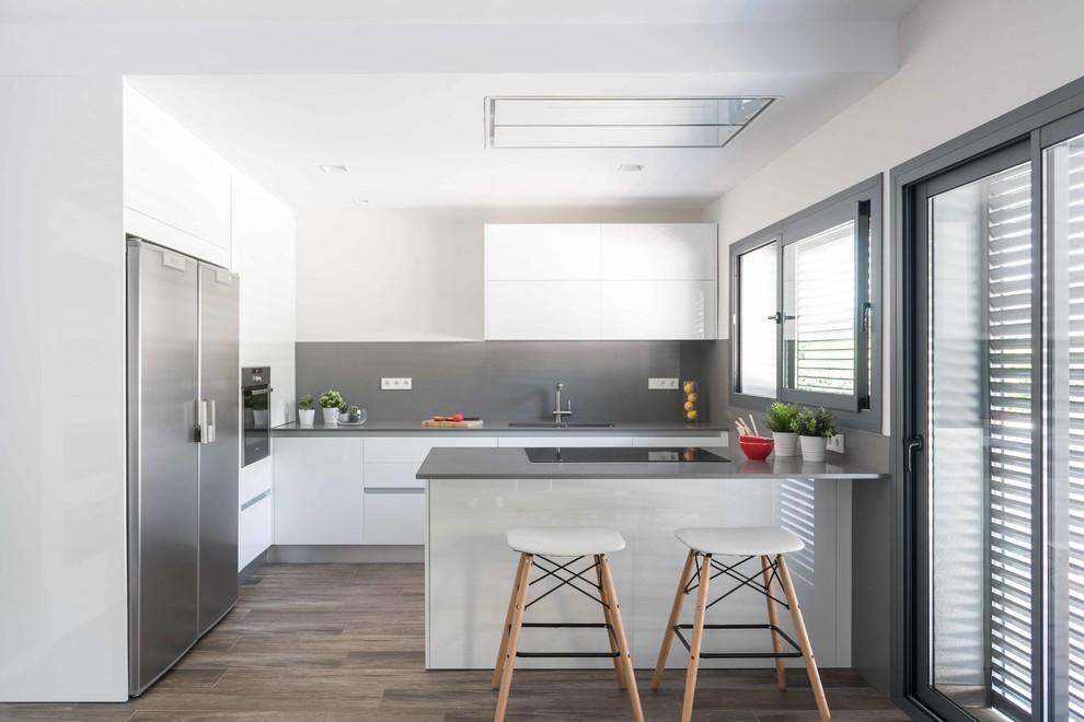 Design ideas for a contemporary kitchen in Barcelona with flat-panel cabinets, white cabinets, grey splashback, stainless steel appliances, dark hardwood floors, a peninsula, grey benchtop, a double-bowl sink and brown floor.