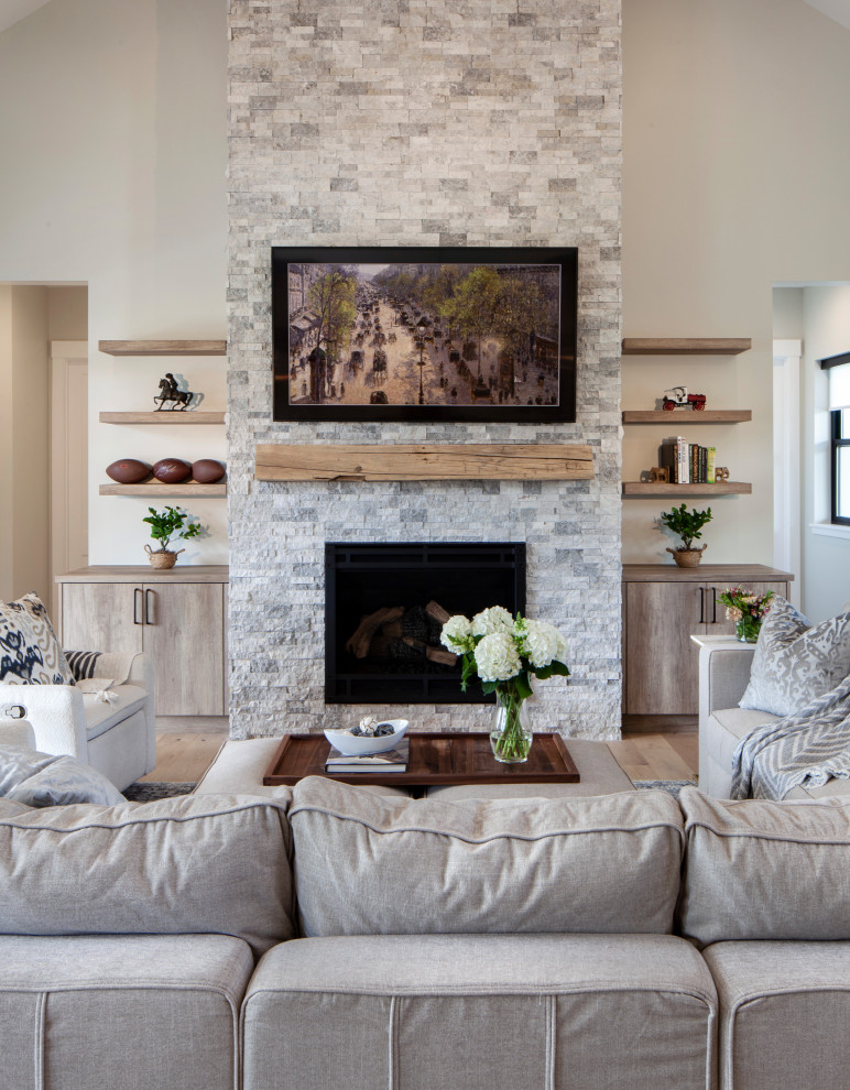 This is an example of a large rural open plan living room in Denver with grey walls, light hardwood flooring, a standard fireplace, a stacked stone fireplace surround, a wall mounted tv, brown floors and a vaulted ceiling.