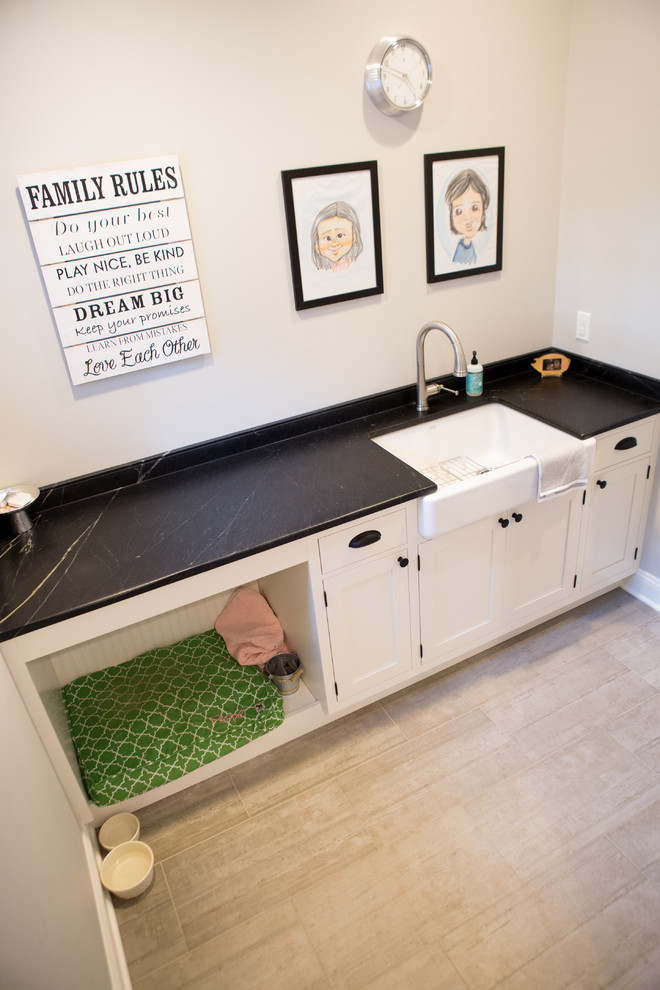 Mid-sized traditional single-wall utility room in New York with a farmhouse sink, beaded inset cabinets, white cabinets, soapstone benchtops, grey walls, porcelain floors and black benchtop.