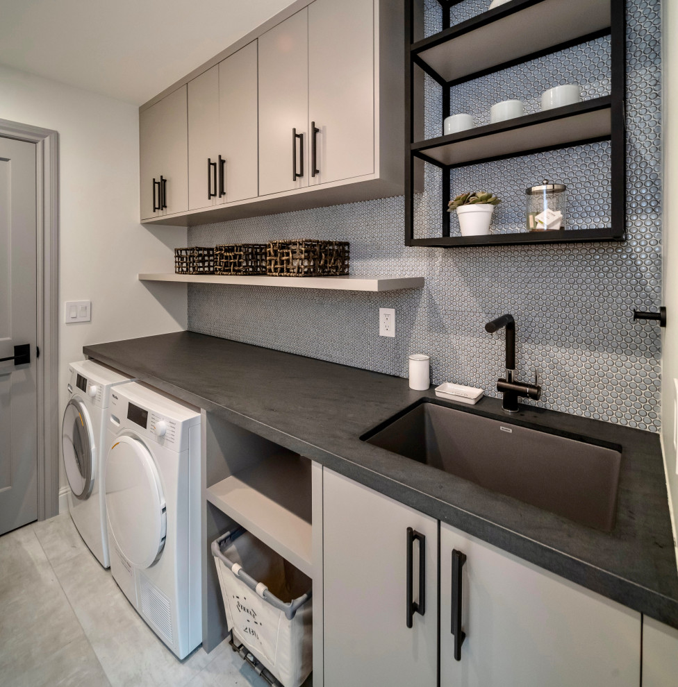 This is an example of a contemporary single-wall dedicated laundry room in San Francisco with an undermount sink, flat-panel cabinets, grey cabinets, quartz benchtops, blue splashback, mosaic tile splashback, white walls, porcelain floors, a side-by-side washer and dryer, grey floor and grey benchtop.