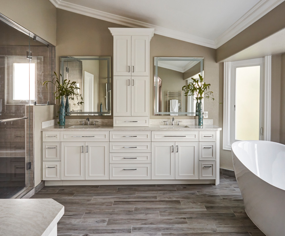 This is an example of a large transitional master bathroom in San Francisco with recessed-panel cabinets, white cabinets, a freestanding tub, a corner shower, a one-piece toilet, brown tile, ceramic tile, beige walls, ceramic floors, an undermount sink, engineered quartz benchtops, brown floor, a hinged shower door and white benchtops.