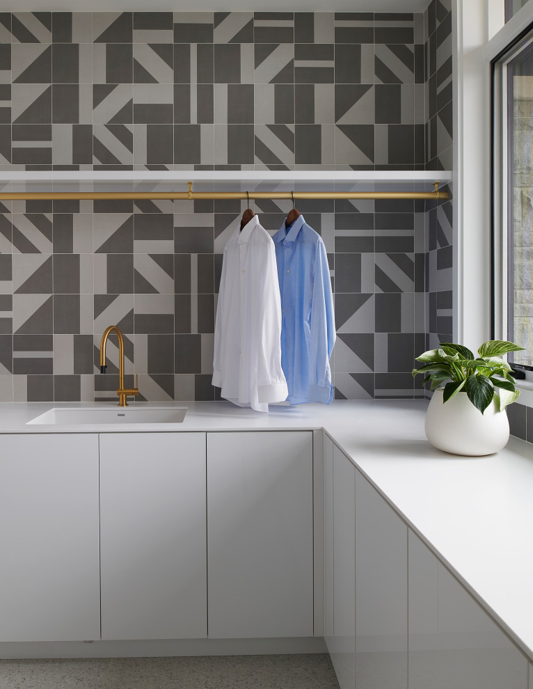 Example of a large trendy u-shaped porcelain tile and white floor dedicated laundry room design in Toronto with an undermount sink, flat-panel cabinets, white cabinets, solid surface countertops, gray backsplash, porcelain backsplash, white walls, a side-by-side washer/dryer and white countertops