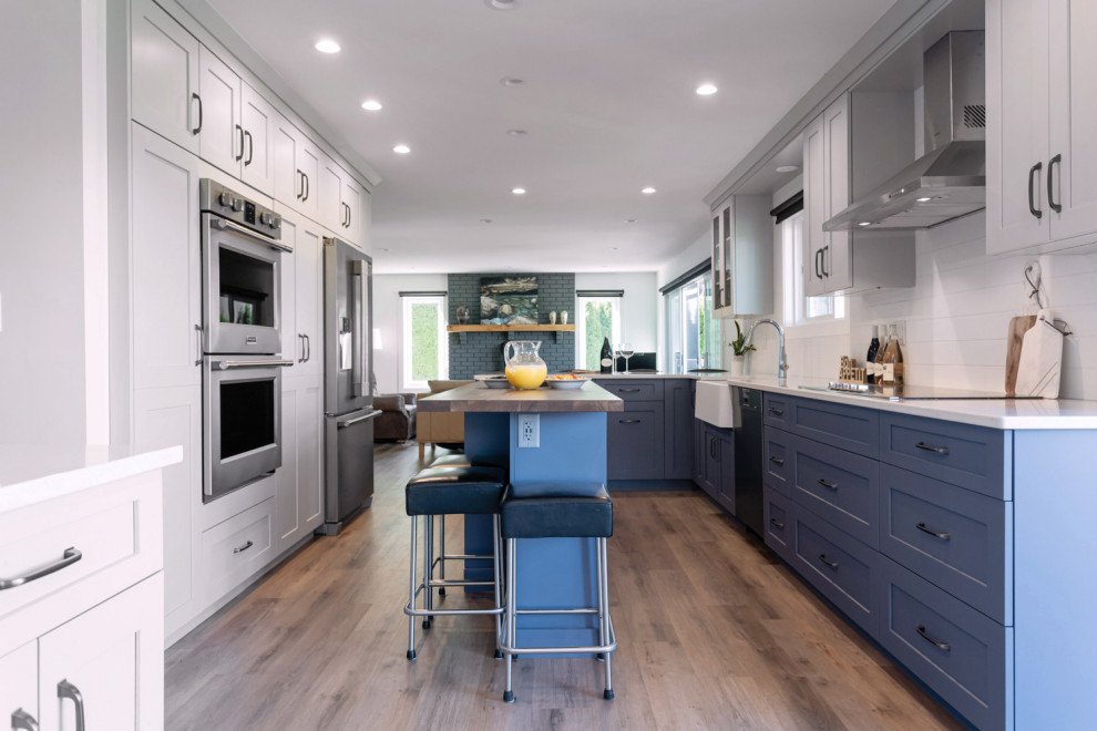 Example of a mid-sized transitional u-shaped medium tone wood floor and brown floor eat-in kitchen design with recessed-panel cabinets, gray cabinets, quartz countertops, white backsplash, ceramic backsplash, stainless steel appliances, an island and white countertops