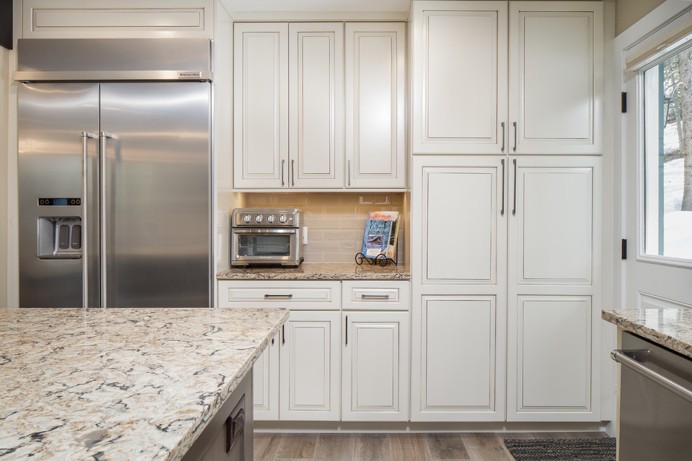 Photo of a mid-sized contemporary u-shaped kitchen in Denver with a farmhouse sink, shaker cabinets, white cabinets, quartz benchtops, white splashback, subway tile splashback, stainless steel appliances, medium hardwood floors and with island.