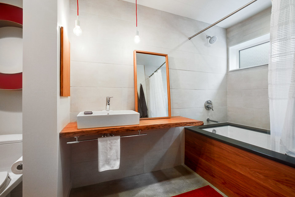 Mid-sized arts and crafts 3/4 bathroom in Seattle with open cabinets, light wood cabinets, an undermount tub, a shower/bathtub combo, a one-piece toilet, gray tile, porcelain tile, white walls, concrete floors, a vessel sink and wood benchtops.