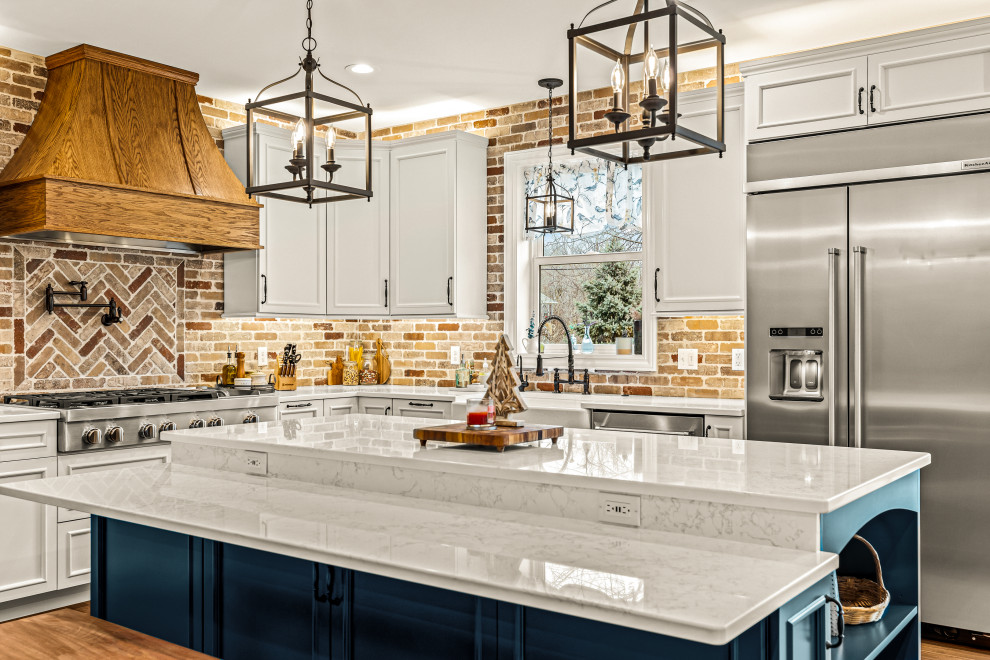 Mid-sized country l-shaped eat-in kitchen in Detroit with a farmhouse sink, recessed-panel cabinets, white cabinets, quartz benchtops, red splashback, brick splashback, stainless steel appliances, light hardwood floors, with island, brown floor and white benchtop.