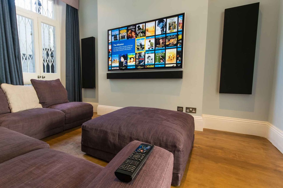 This is an example of a contemporary enclosed home theatre in London with blue walls, medium hardwood floors, a wall-mounted tv and brown floor.