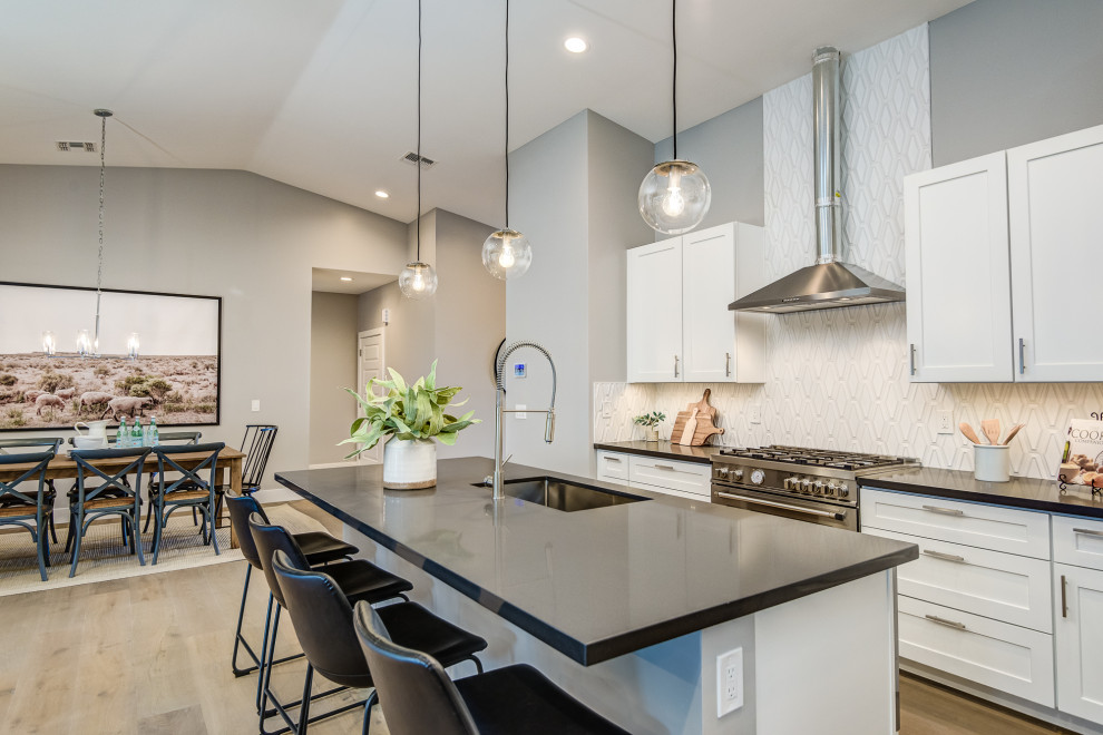 Inspiration for a transitional galley medium tone wood floor and brown floor kitchen remodel in Phoenix with an undermount sink, shaker cabinets, white cabinets, white backsplash, stainless steel appliances, an island and black countertops